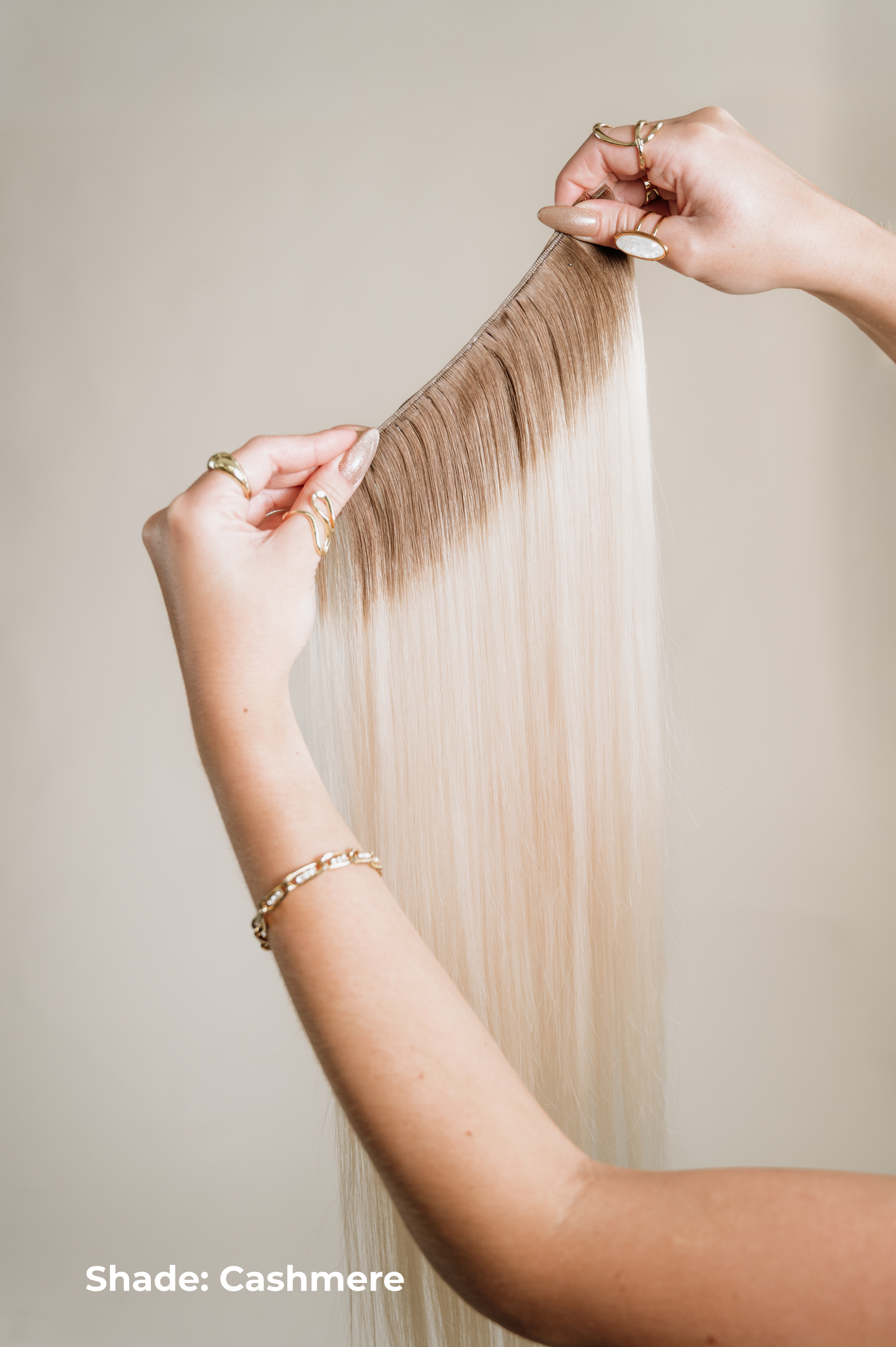 Person holding a strand of blonde hair extensions with 'Shade: Cashmere' text on a neutral background