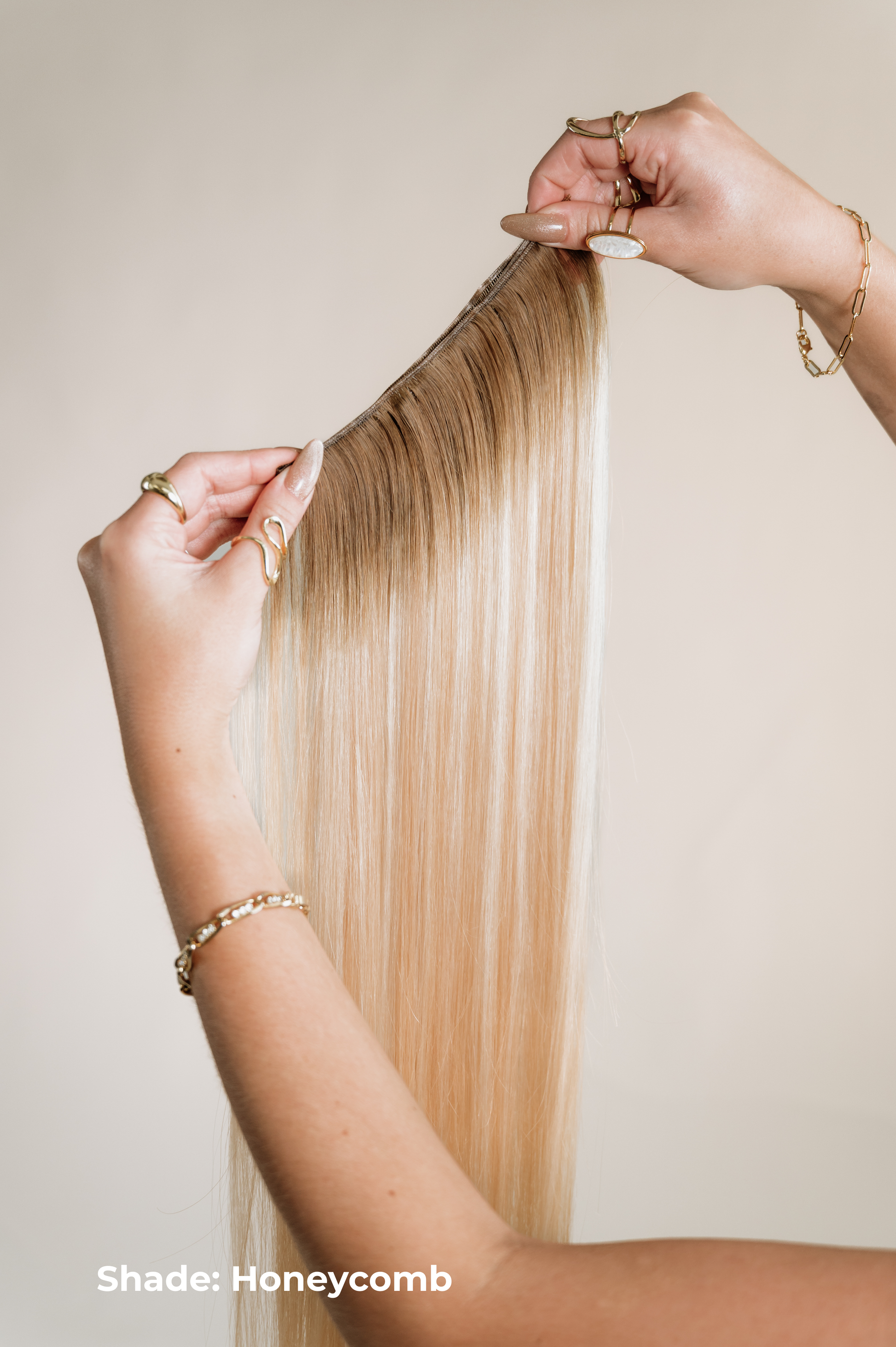 Blonde hair extensions held by hands against a neutral background